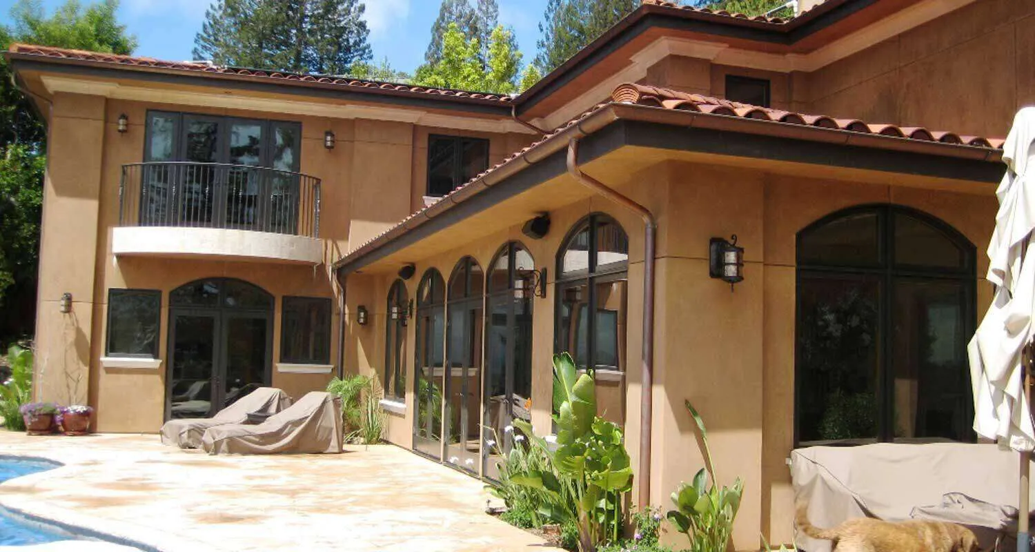 Two-story home with cementitious finish, arched windows, and a balcony, viewed from a poolside patio.