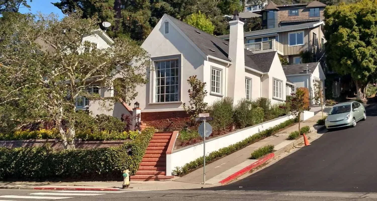 White stucco house with brick stairs and landscaping on a sloped street in San Rafael.