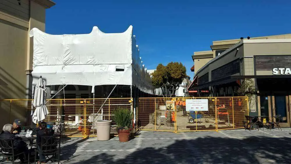 Commercial building covered with white tarp and surrounded by yellow fencing, indicating EIFS work in progress.