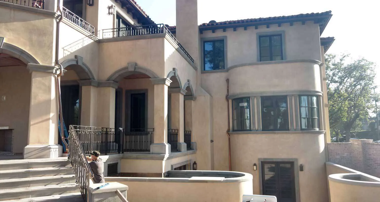 Large residential building with smooth stucco finish and arched details, person working on railing.