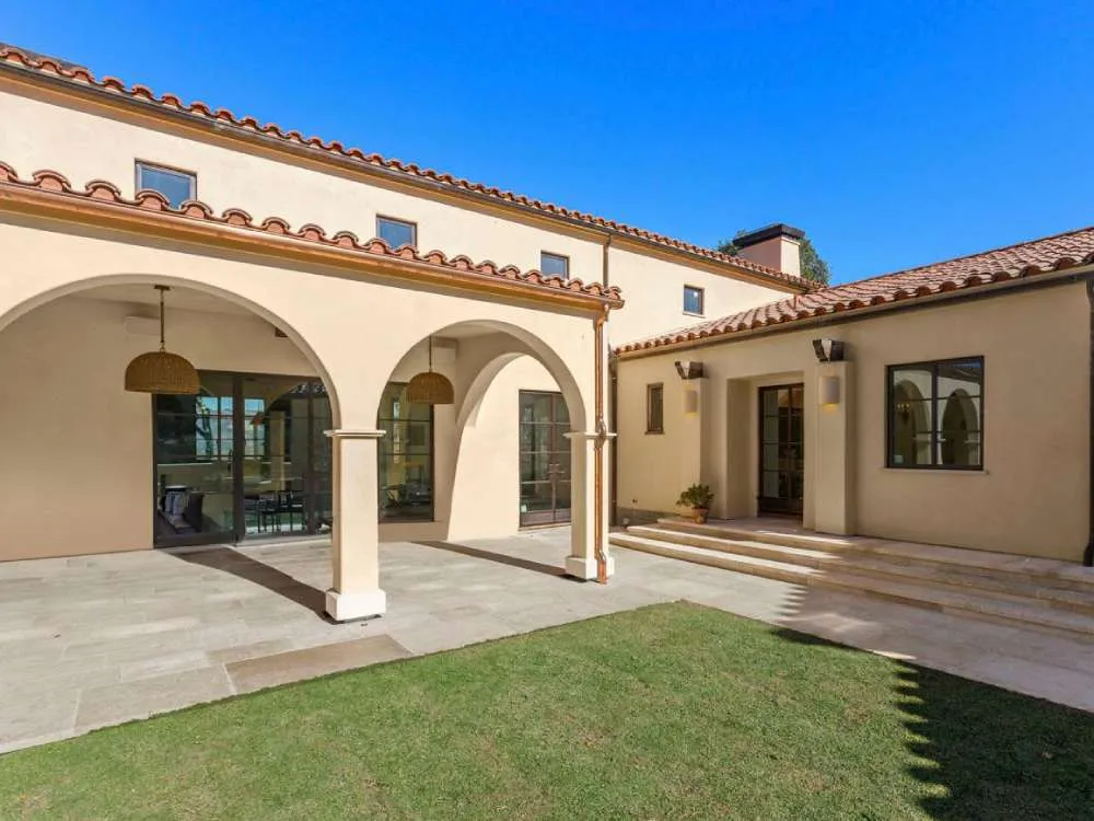 Mediterranean-style courtyard with stucco walls, arched columns, and tiled roof under a clear blue sky.