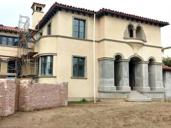 Mediterranean-style two-story home with stucco exterior and scaffolding on the side.