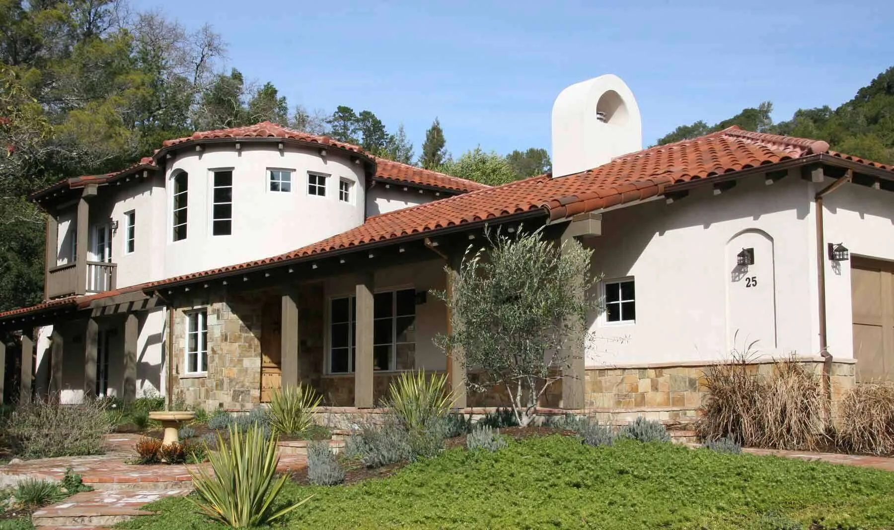 Mediterranean-style home with stucco walls, red tile roof, and arched windows in a lush setting.
