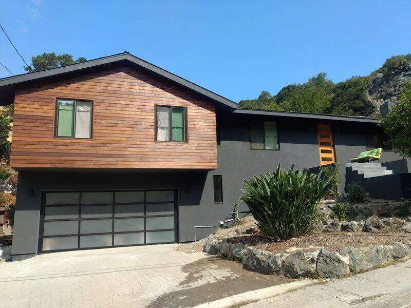 Modern single-family home with dark stucco and wood siding, large garage, and landscaped yard.
