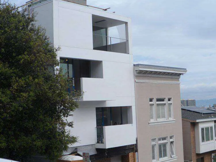 Modern multi-story building with smooth white exterior and large glass windows in an urban setting.