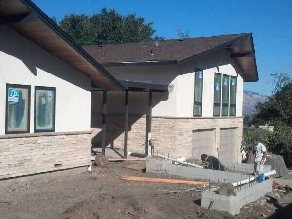 Modern residential home with stucco and stone veneer under construction, workers present.
