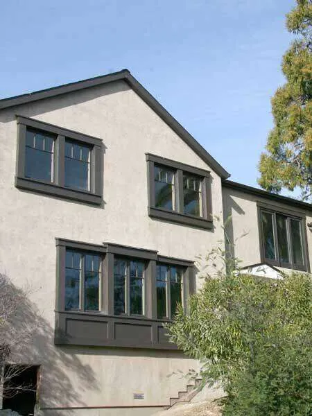 Two-story home with smooth stucco finish and dark-framed windows, surrounded by trees.