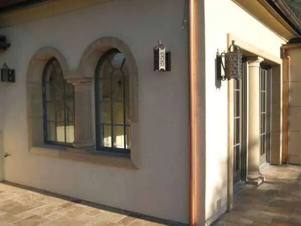 Building exterior with stucco walls, arched stone-framed windows, and decorative sconces.