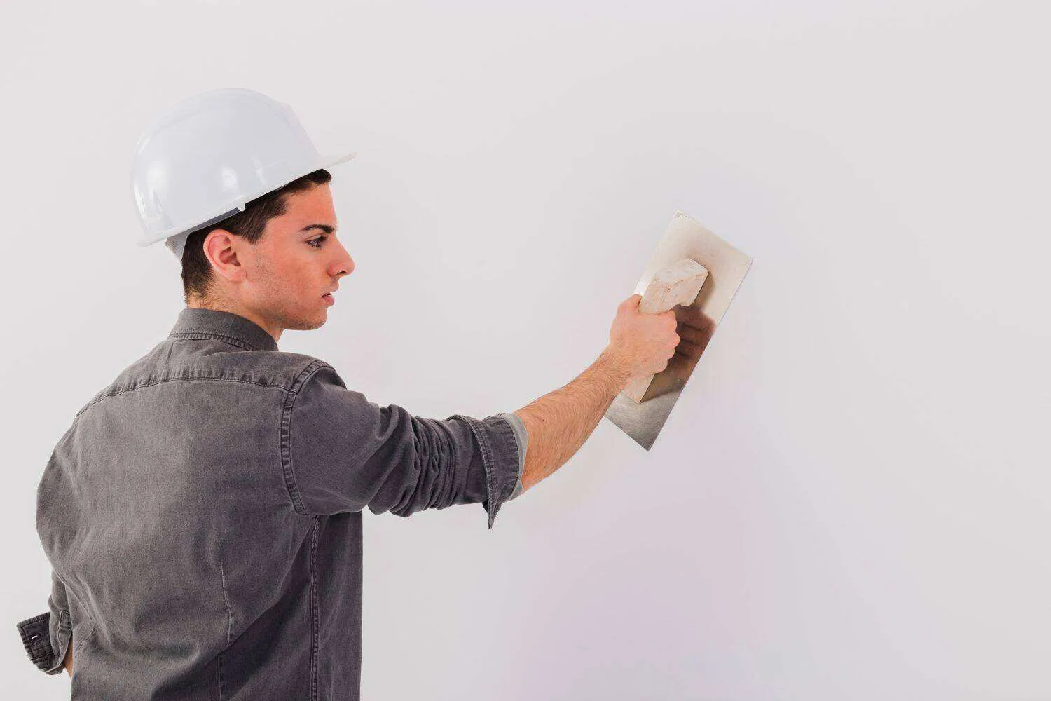 Person in hard hat applying plaster to a white wall with a trowel.