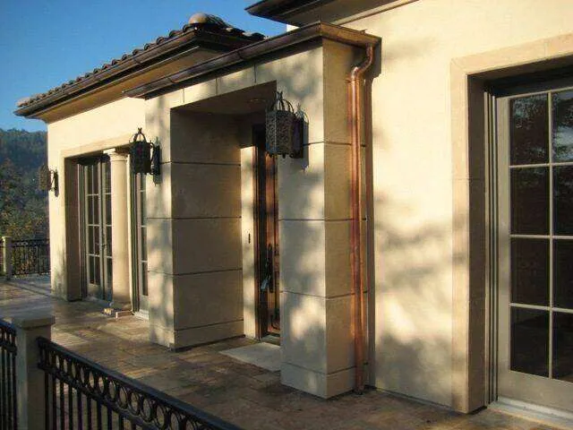 Residential exterior with smooth stucco finish, large windows, and decorative lanterns on a patio.