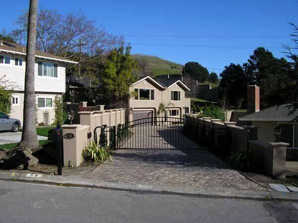 Stucco-finished home with gated driveway and landscaping, set against hills.