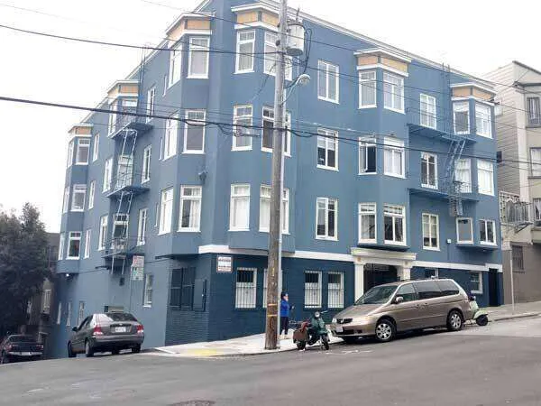 Multi-story blue stucco building with white windows on a sloped street in San Francisco.