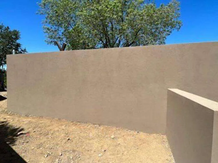 Smooth-finished concrete retaining wall with trees in the background.