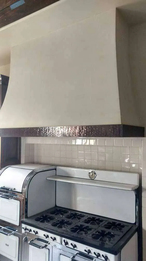 Kitchen with vintage stove and smooth plaster-finished range hood above tiled backsplash.