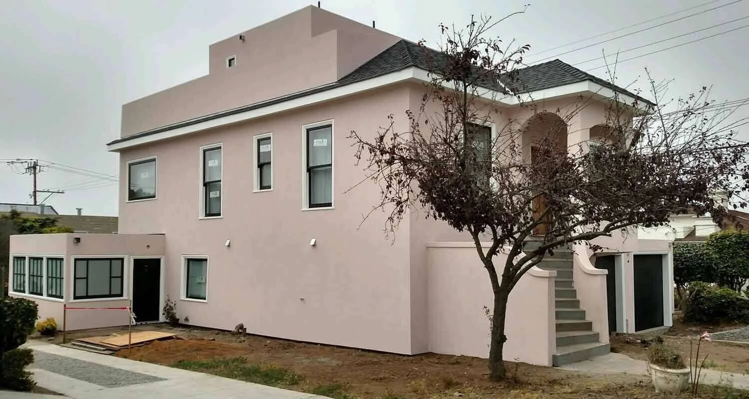 Two-story house with smooth pink stucco finish, multiple windows, and a front staircase.