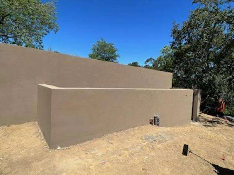 Newly constructed smooth stucco retaining wall in an outdoor area with trees.