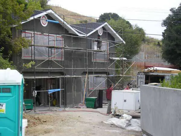 Two-story house with scaffolding and workers applying stucco to the exterior walls.