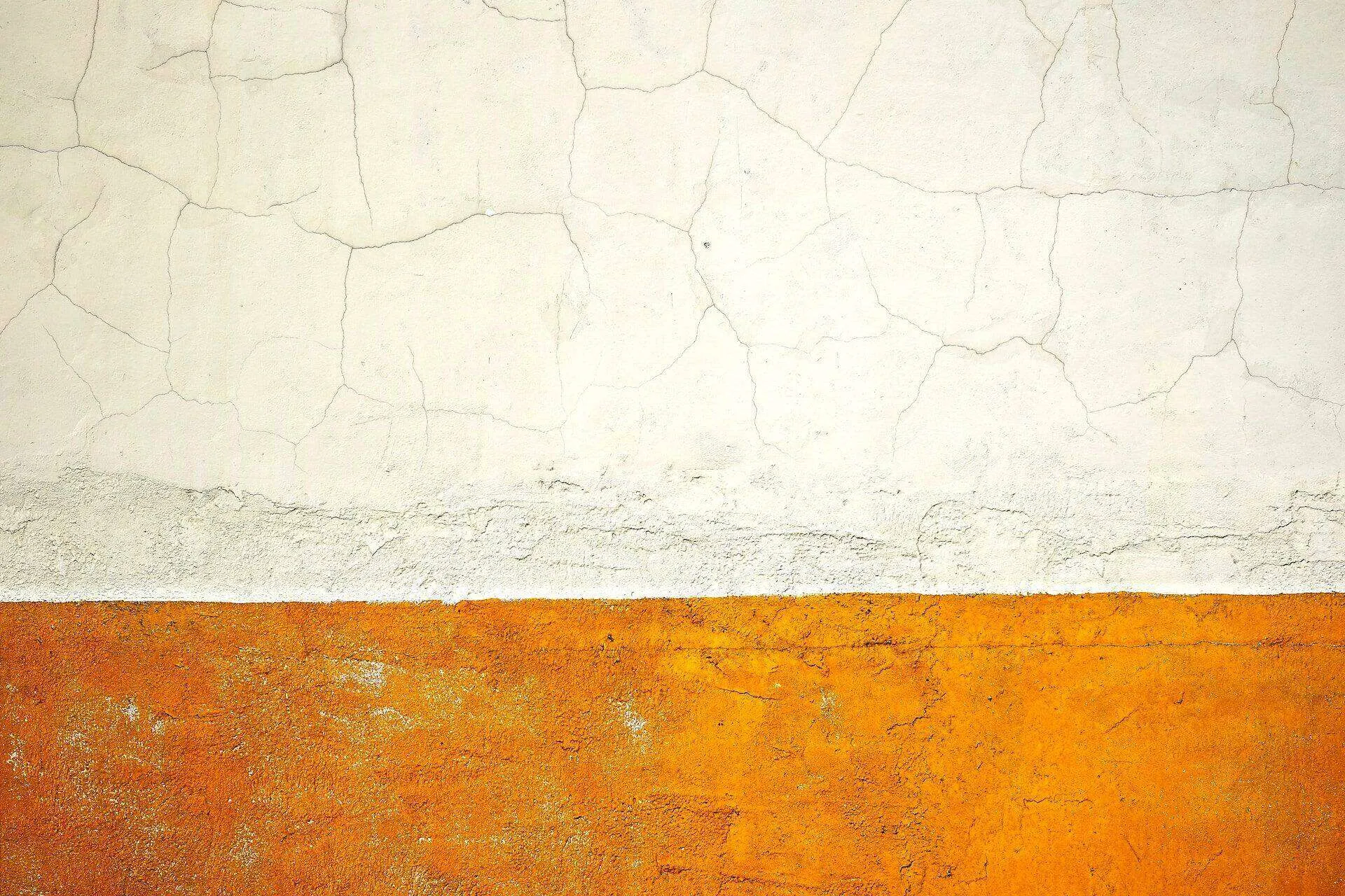 Wall with cracked white stucco above and textured orange stucco below.