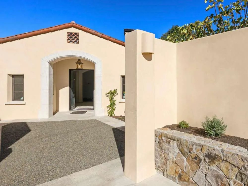 Stucco building exterior with arched entrance and stone wall planter under clear blue sky.