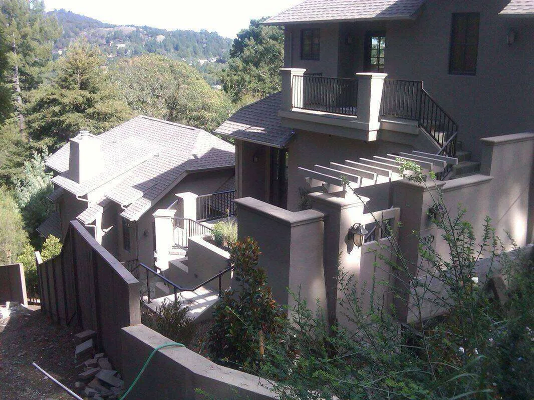 Multi-level home with stucco walls, tiled roof, and hillside view surrounded by trees.