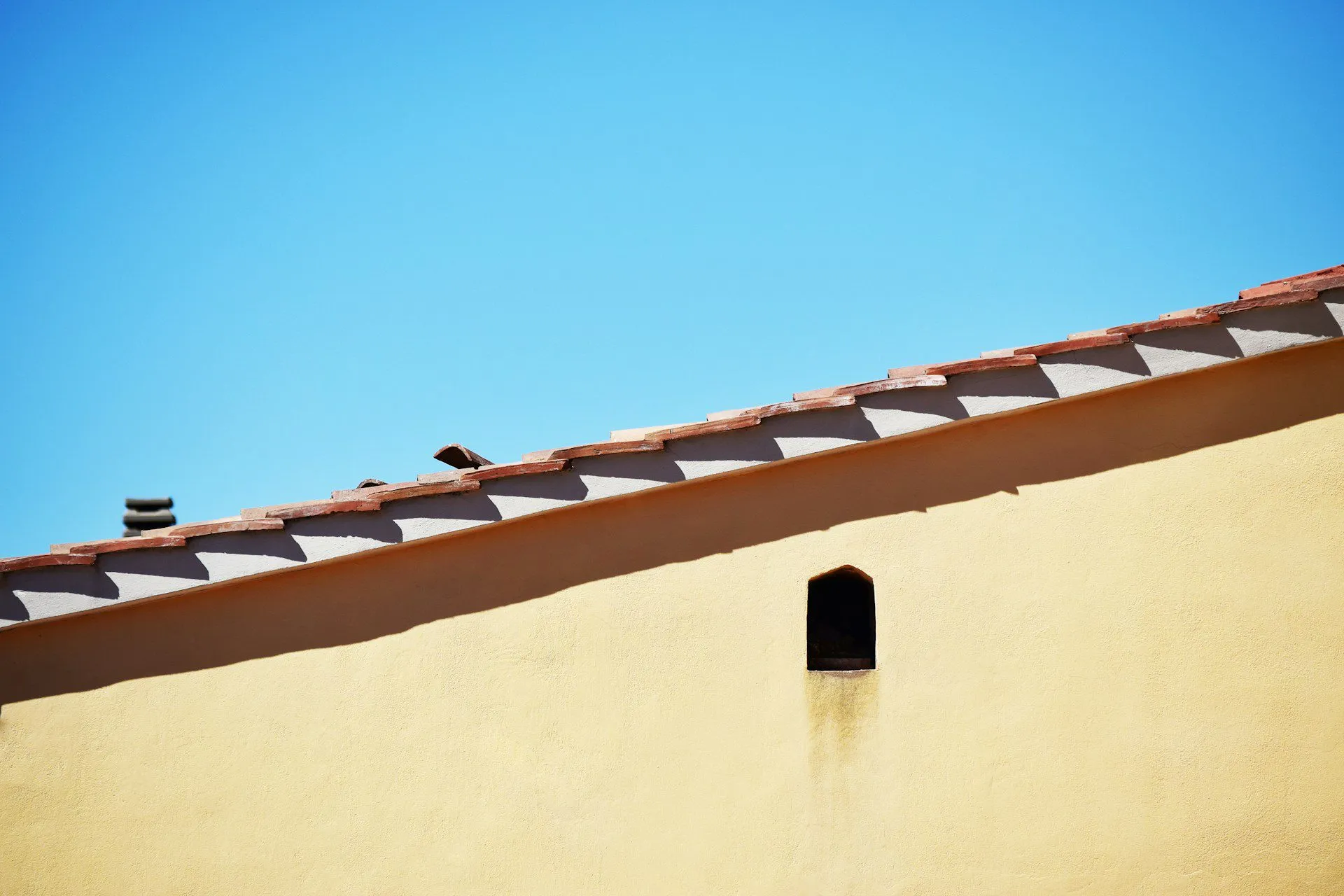 Yellow stucco wall with sloped roof and small vent under a clear blue sky.