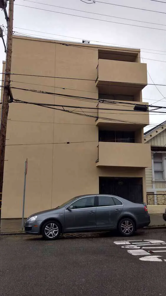 Multi-story building with smooth beige exterior and balconies, car parked in front.