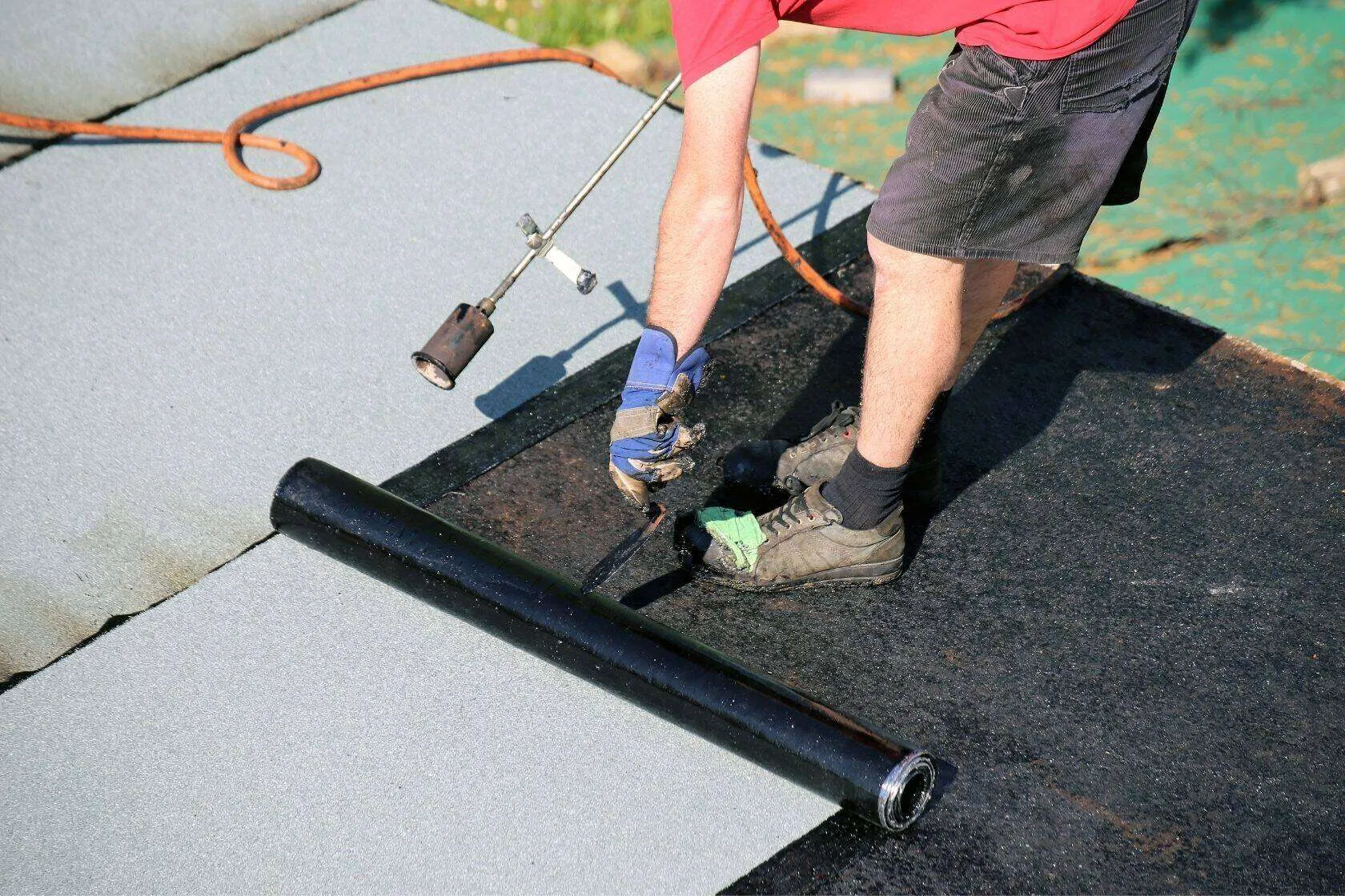 Worker applying waterproofing membrane with a torch on a flat surface.