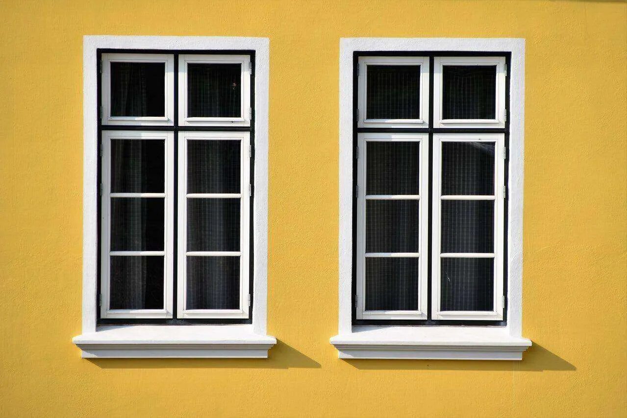 Two white-framed windows on a bright yellow stucco wall with multiple panes.